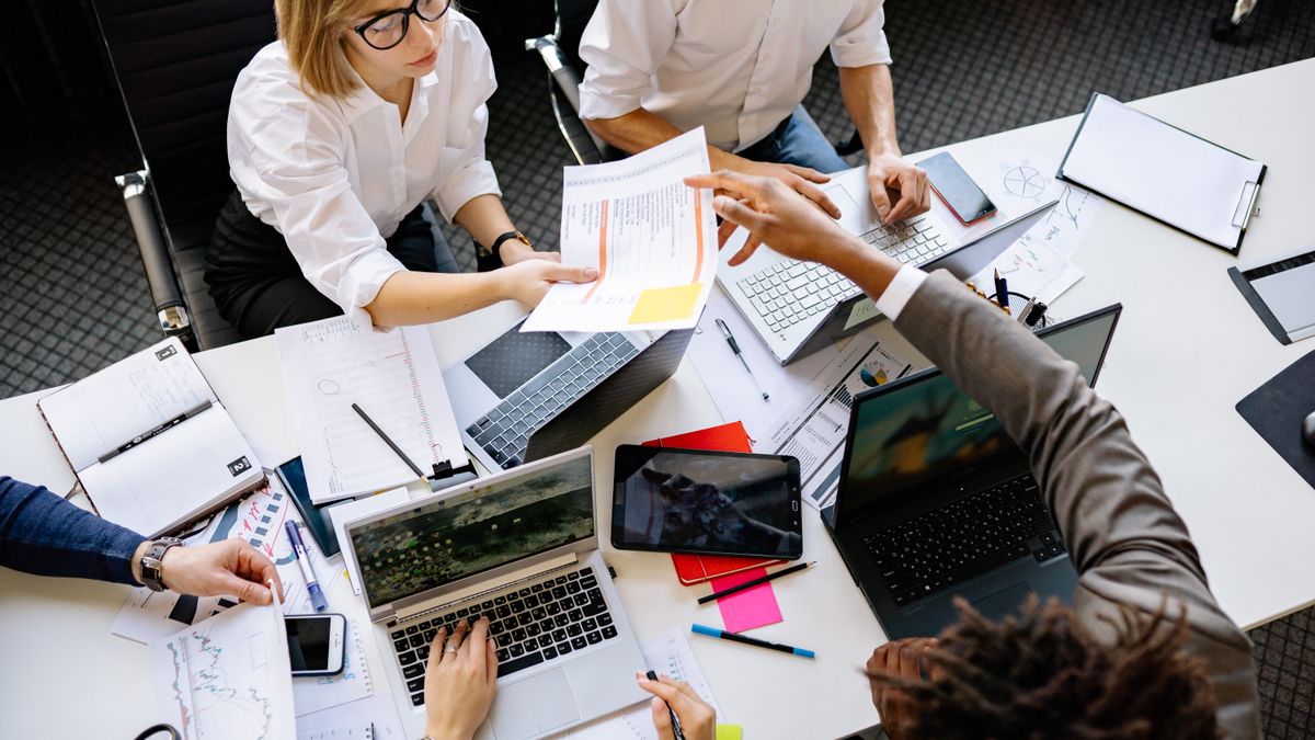 Diverse team collaborating in a modern office with laptops and documents.