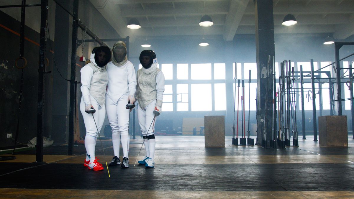 Three athletes in fencing gear standing indoors with swords ready for practice.