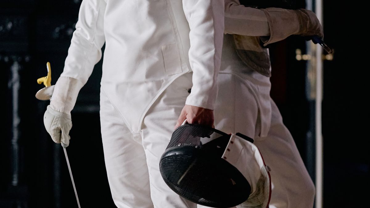 Two fencers in uniform engaged in a competitive fencing match indoors.