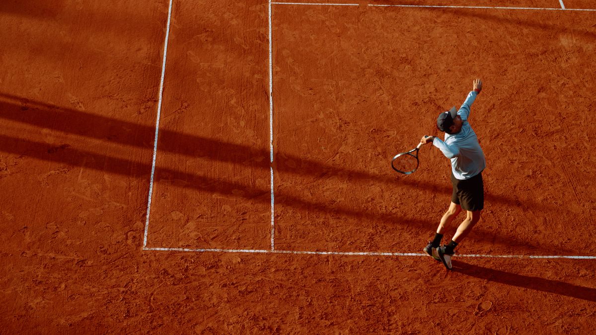 A dynamic shot of a tennis player serving on a clay court during sunset.
