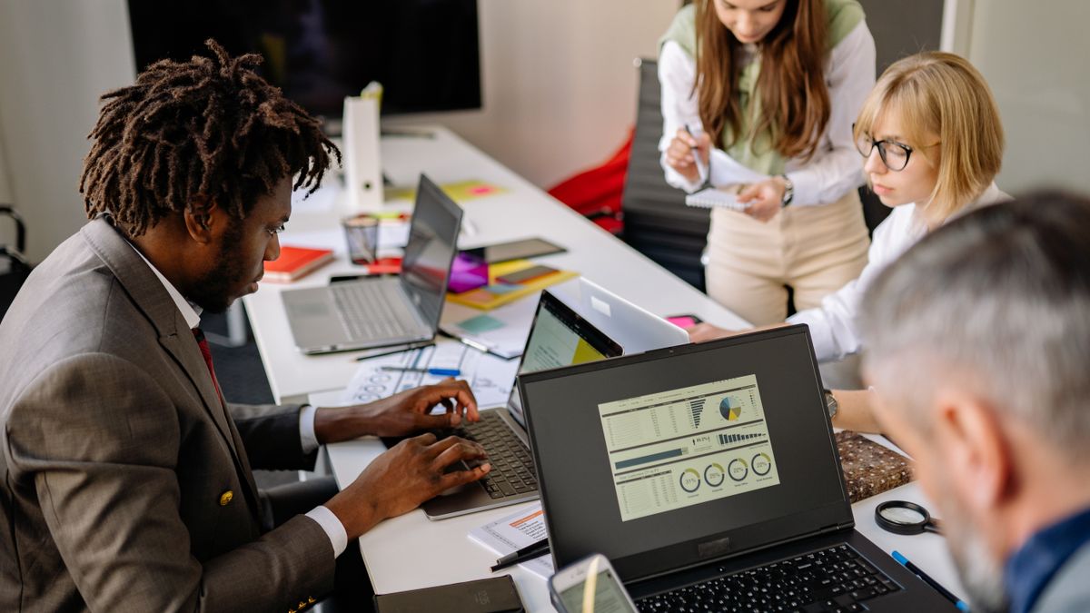 Diverse coworkers engaged in teamwork using laptops and digital devices in a modern office setting.
