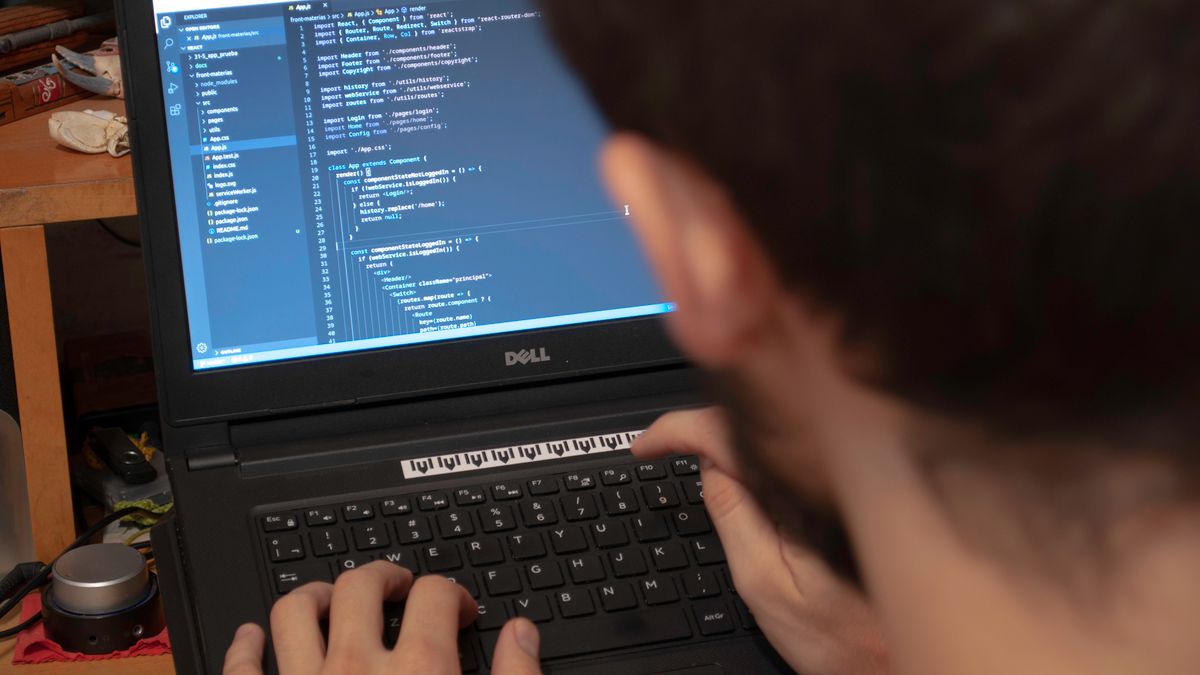 Close-up view of a programmer typing code on a laptop in a workspace.