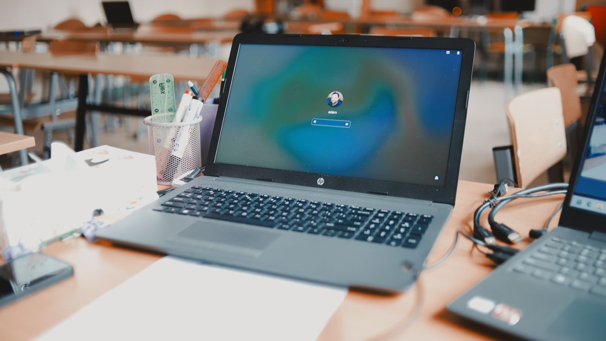 A close-up of a laptop on a desk in a classroom setting, ready for educational use.