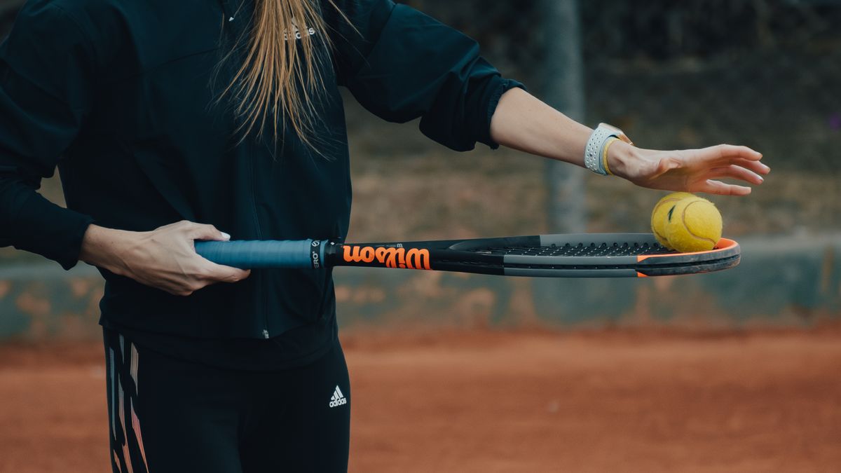 Close-up of a woman holding a tennis racket and ball ready for a serve on a clay court.