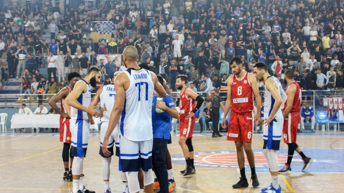 Basketball players in action during a competitive match with a full stadium crowd.